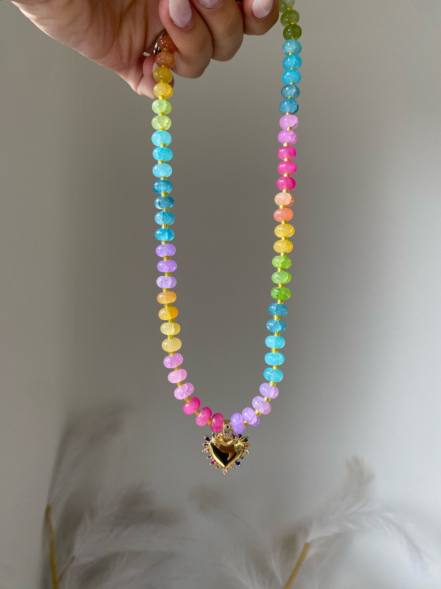 necklace with purple, pink, blue, yellow, and green beads separated by gold spacers, gold heart pendant with sapphire detailing