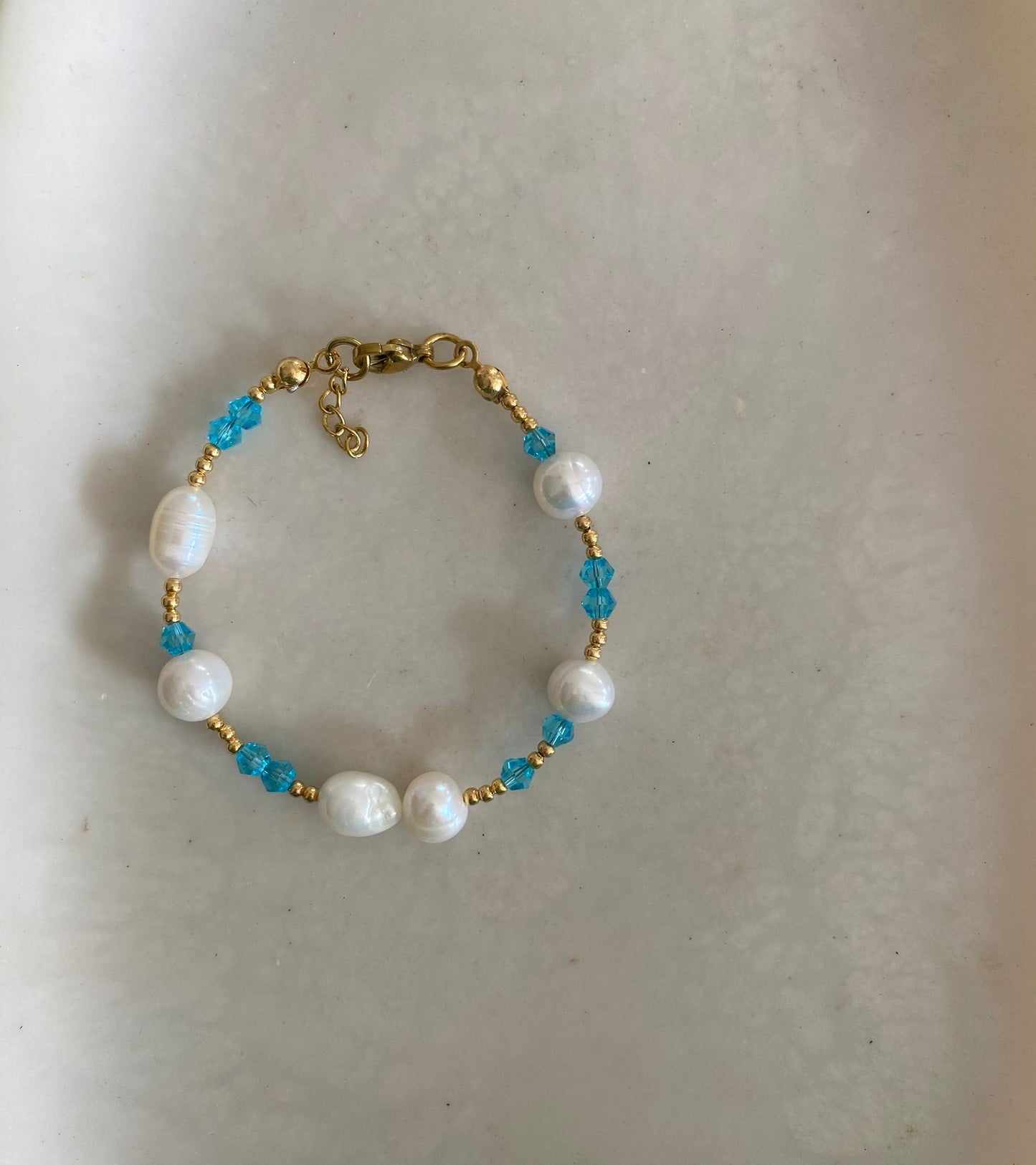 Bracelet with freshwater pearls, aqua blue crystal bicone beads, and gold seed beads, laid flat on a marble dish