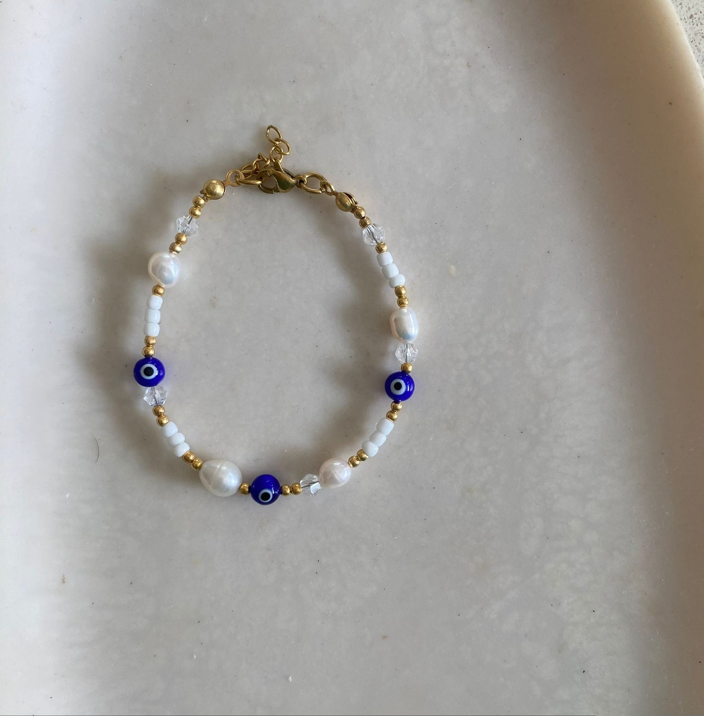Gold beaded bracelet with freshwater pearls, white seed beads with clear crystal accents, and cobalt blue evil eye charm beads