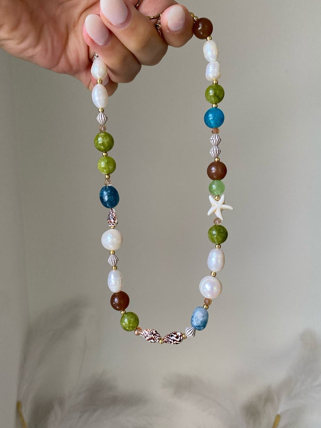 beaded necklace featuring olive green, ocean blue and brown gemstone beads with freshwater pearls, shell beads, a starfish accent and gold seed spacers