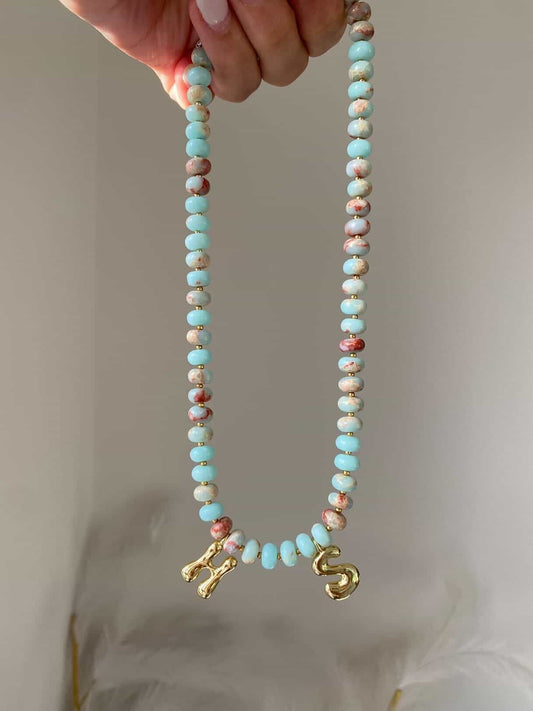 The Tilly necklace with two gold letter initial charms, H and S, separated by 6 beads at the centre
