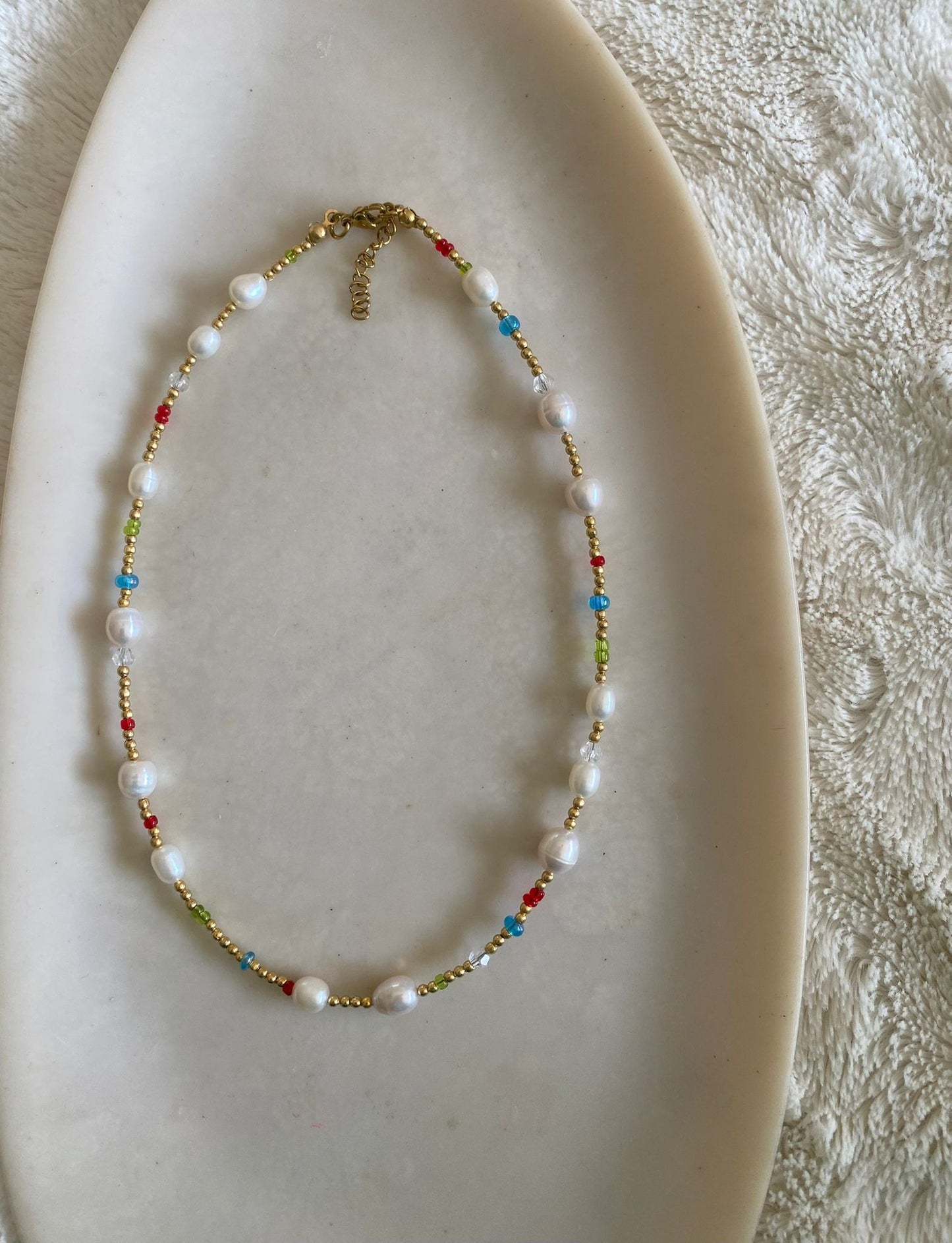 Beaded necklace with gold seed beads, freshwater pearls, and multicolour seed bead accents in red, blue, and green, laid flat on a marble dish