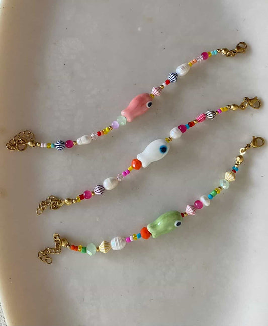 Three colourful sea-themed beaded bracelets with ceramic fish focal beads in pink, white, and green, mixed multicolour seed beads and gold lobster clasps
