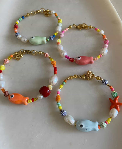 Four colourful sea-themed beaded bracelets with ceramic fish and starfish focal beads in mint green, pink, orange, and blue, mixed multicolour seed beads and gold clasps.