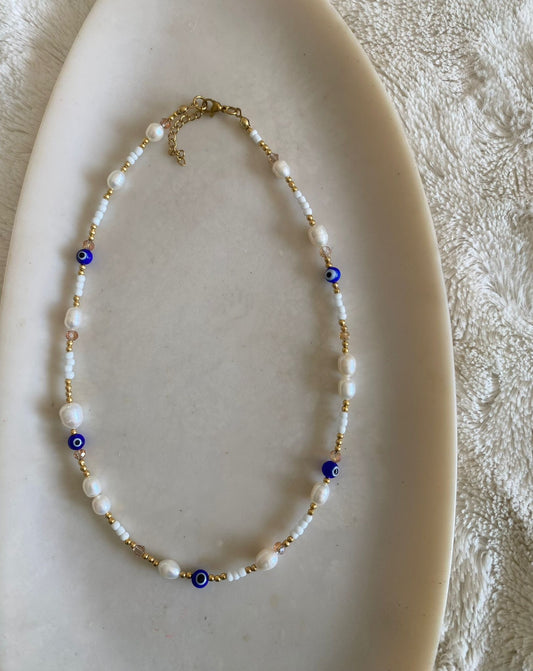 beaded necklace featuring freshwater pearls, white seed beads and blush pink crystal accents with cobalt blue evil eye charm beads and gold seed spacers