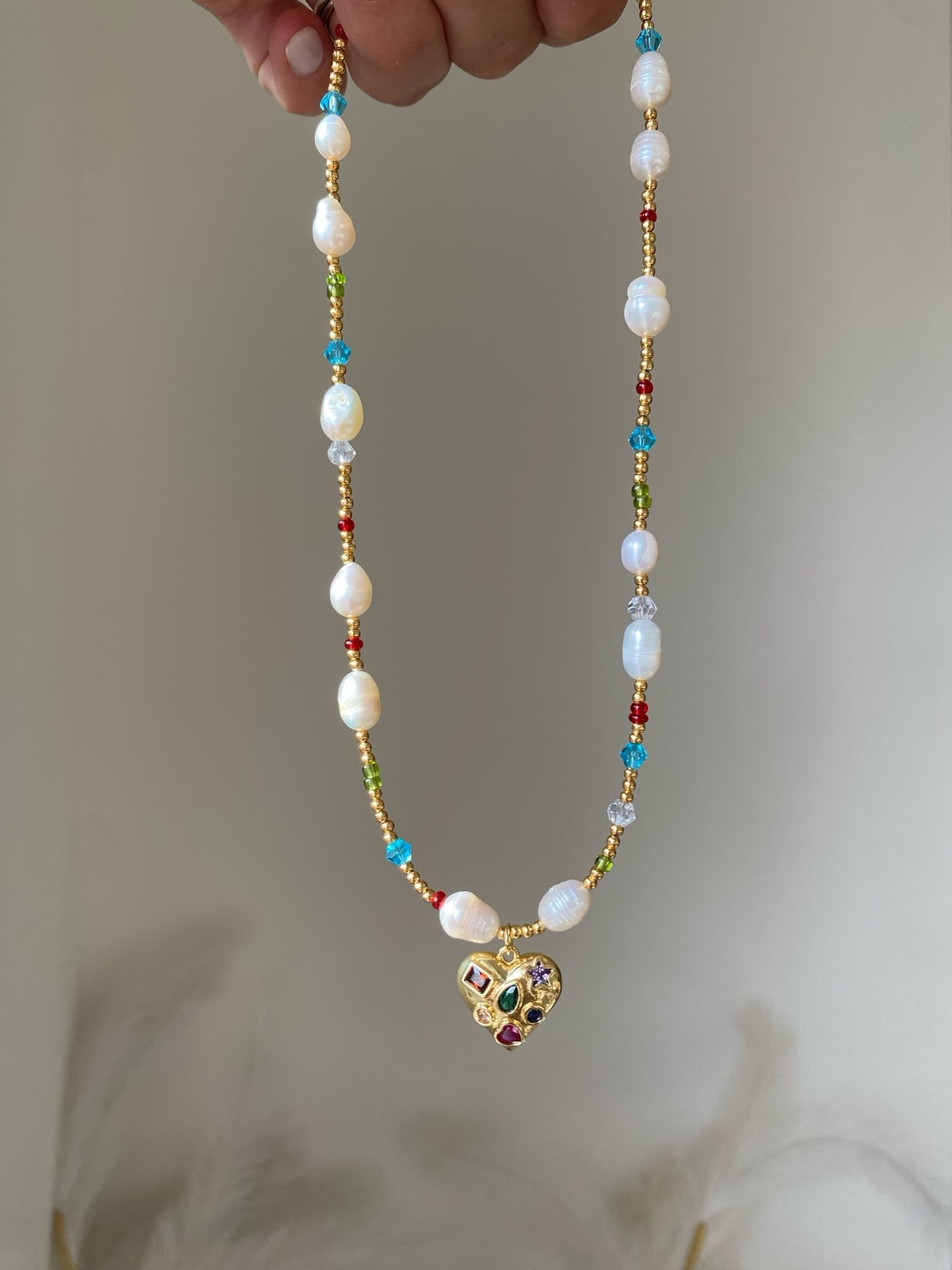 Gold beaded necklace with freshwater pearls and red, green and blue crystal accents and a gold gemstone-studded heart pendant