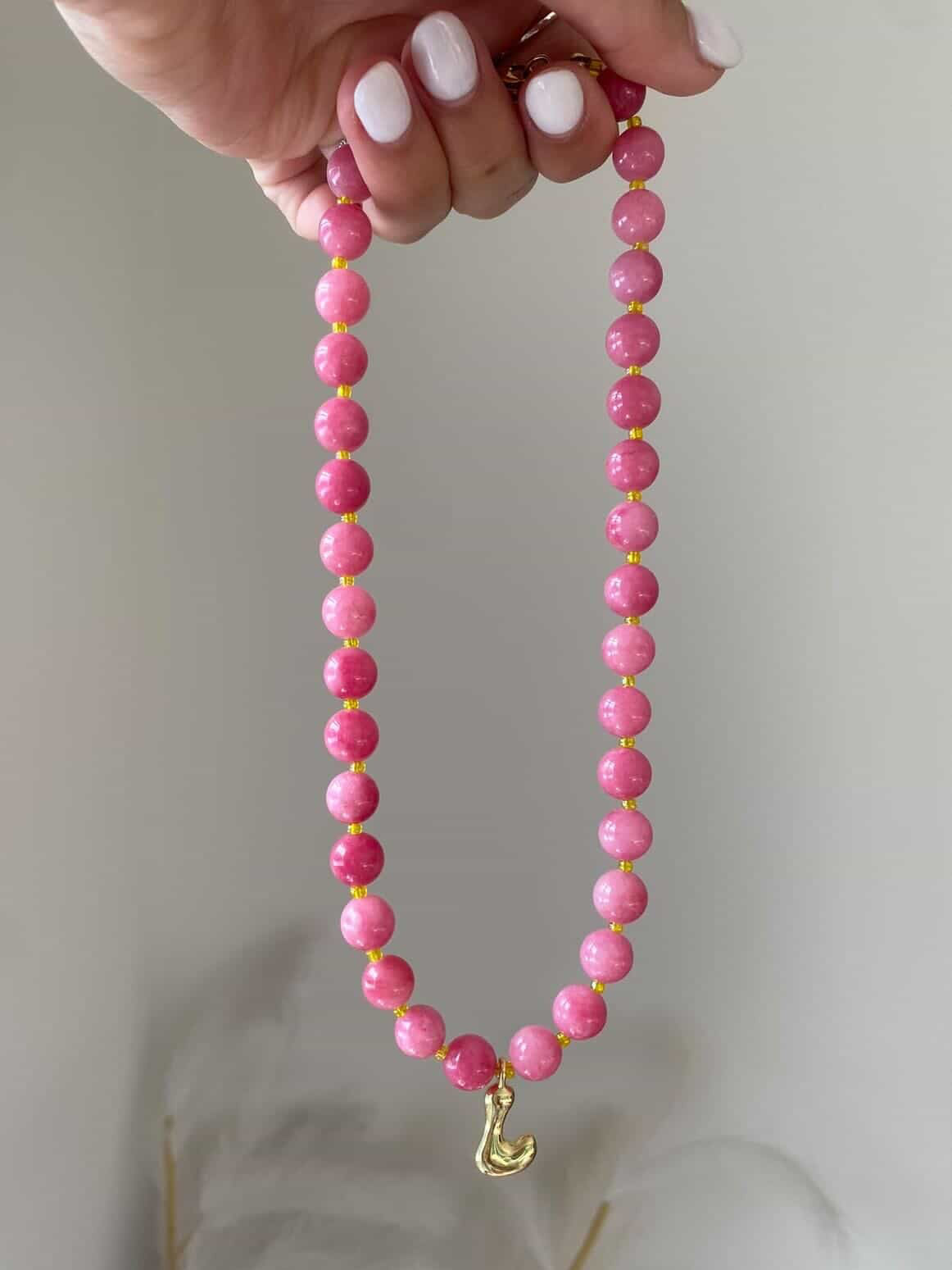 A coral pink round beaded necklace with gold spacers and a single gold bubble letter L charm