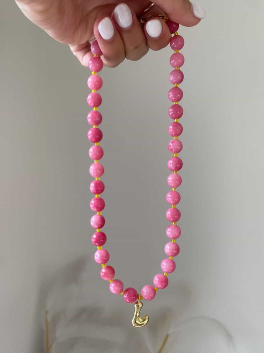 A coral pink round beaded necklace with gold spacers and a single gold bubble letter L charm