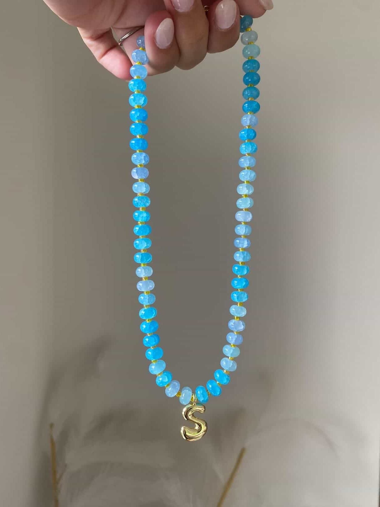 A bright blue and ice blue ombre beaded necklace with gold spacers and a single gold bubble letter S charm