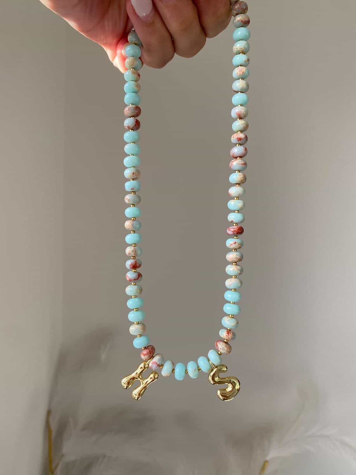 The Tilly necklace with two gold letter initial charms, H and S, separated by 6 beads at the centre