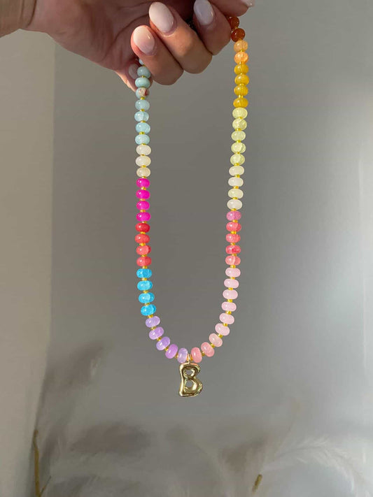 A multicoloured beaded necklace with tones of pale blue, lilac, pinks, yellows, and corals, separated by spacer beads. A gold bubble initial B hanging from the centre