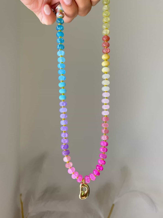 A multicoloured beaded necklace with tones of blue, lilac, pinks, yellows, and corals, separated by spacer beads. A gold bubble initial D hanging from the centre.