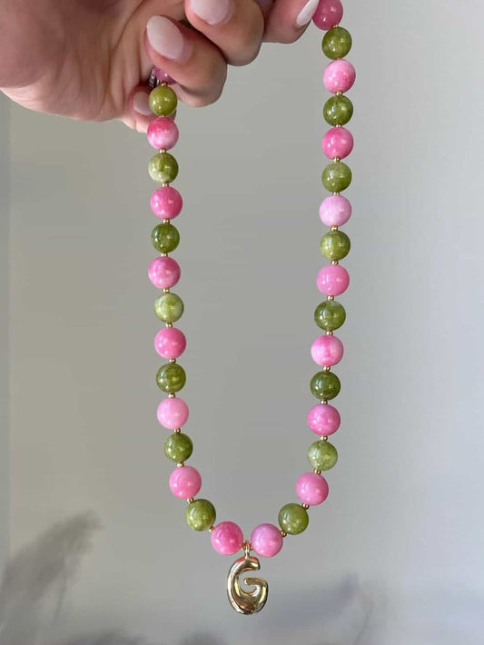 Beaded necklace with large hot pink and olive green gemstone beads, gold seed spacers, and a gold bubble letter G initial pendant