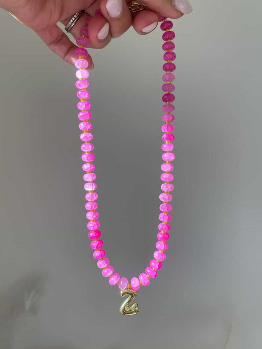A vivid pink beaded necklace with gold spacers and a single gold bubble letter Z charm