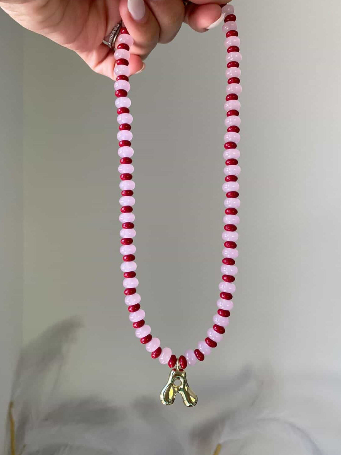 A blush pink and deep red alternating beaded necklace stacked on top of each other, with a single gold bubble letter A charm