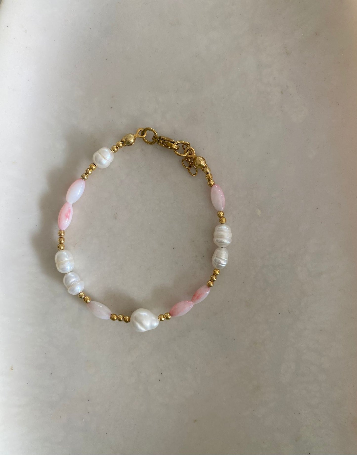 Bracelet with claw clasp, freshwater pearls, blush pink oval beads, and gold seed beads, laid flat on a marble dish