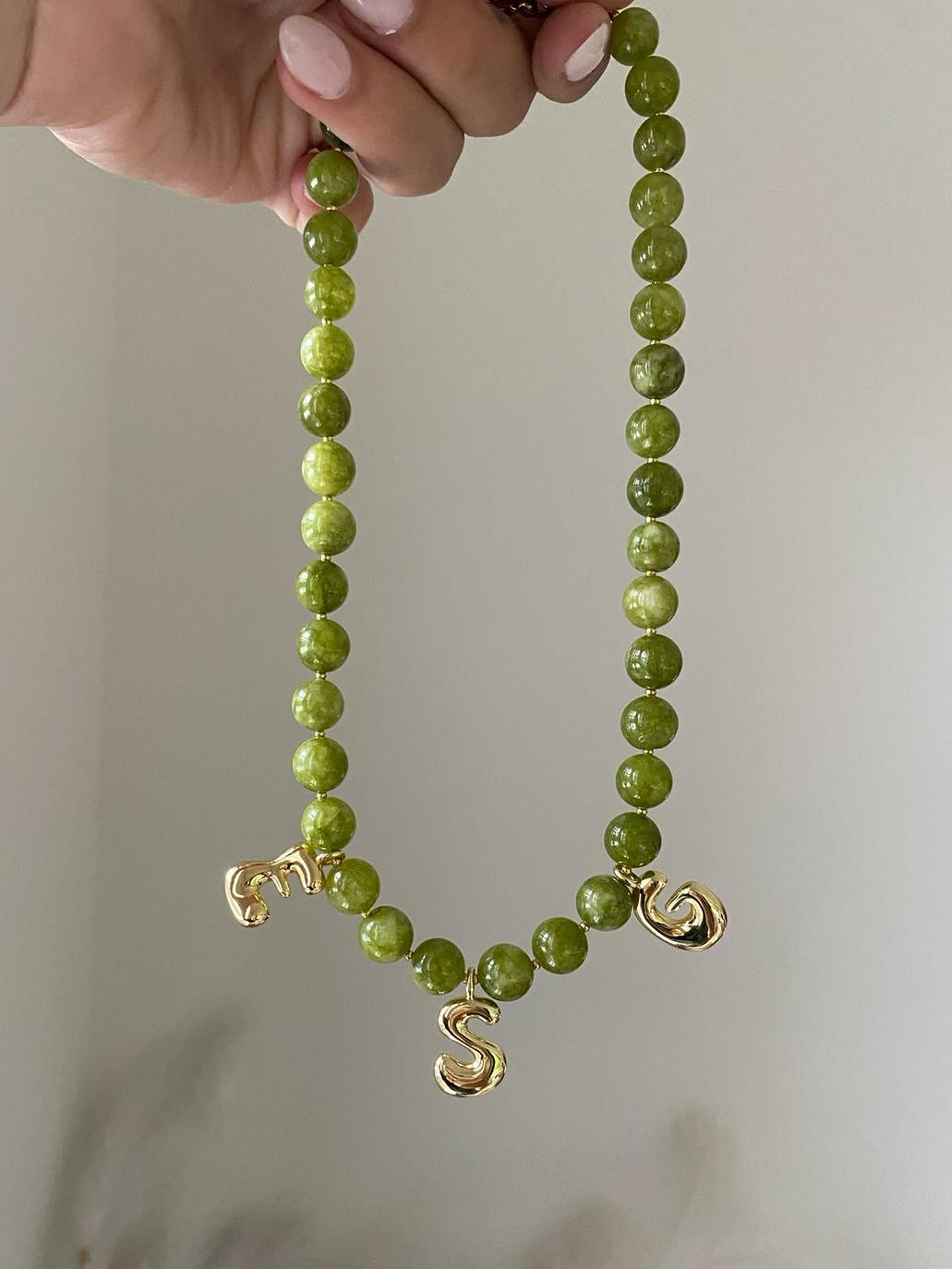 A green beaded necklace, each bead is separated by a gold spacer. 3 initial bubble letters, e s and g hand 3 beads apart