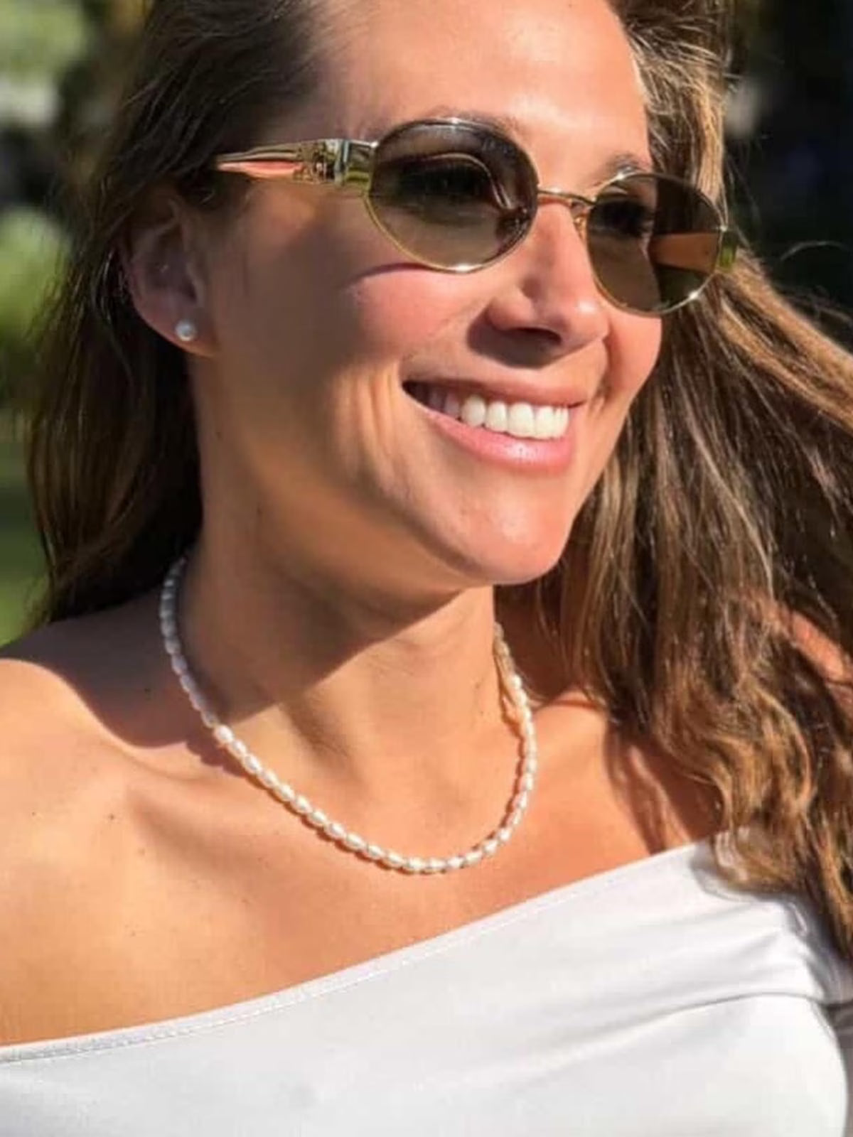 Customer wearing a closely strung freshwater pearl necklace, styled with a white off-shoulder top and gold sunglasses